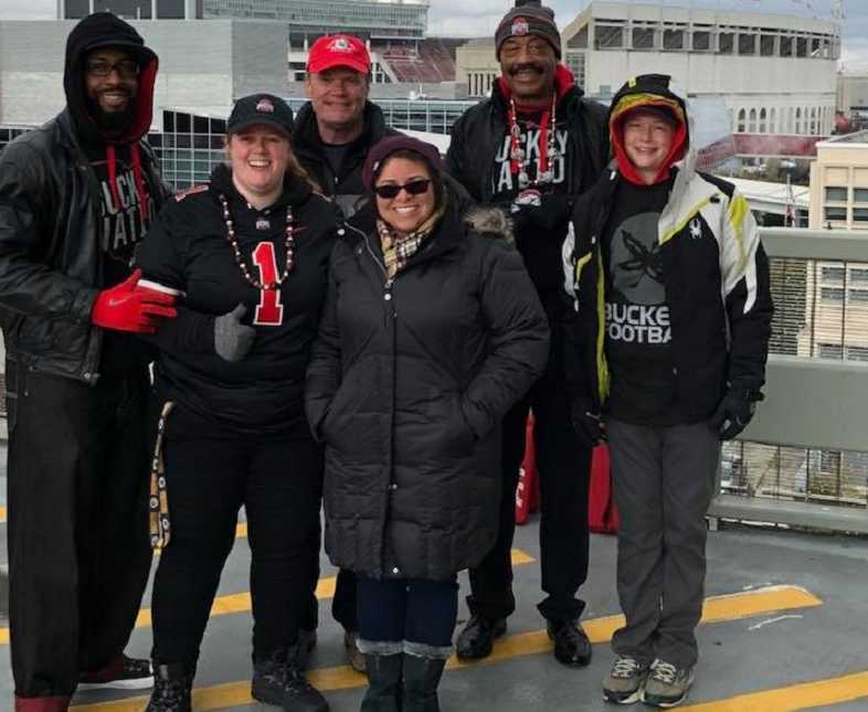 two women and four men smiling in ohio state gear with the football stadium in the background