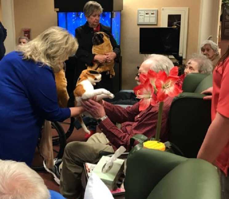red flower blocking the side profile of elderly man sitting and grabbing a stuffed dog from woman 