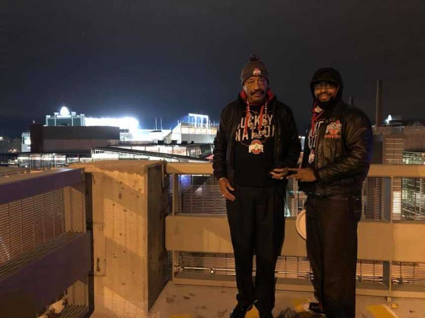 two men in ohio state gear standing at night with football stadium in the background