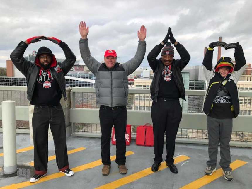 four men spelling out ohio with their arms wearing ohio state gear 