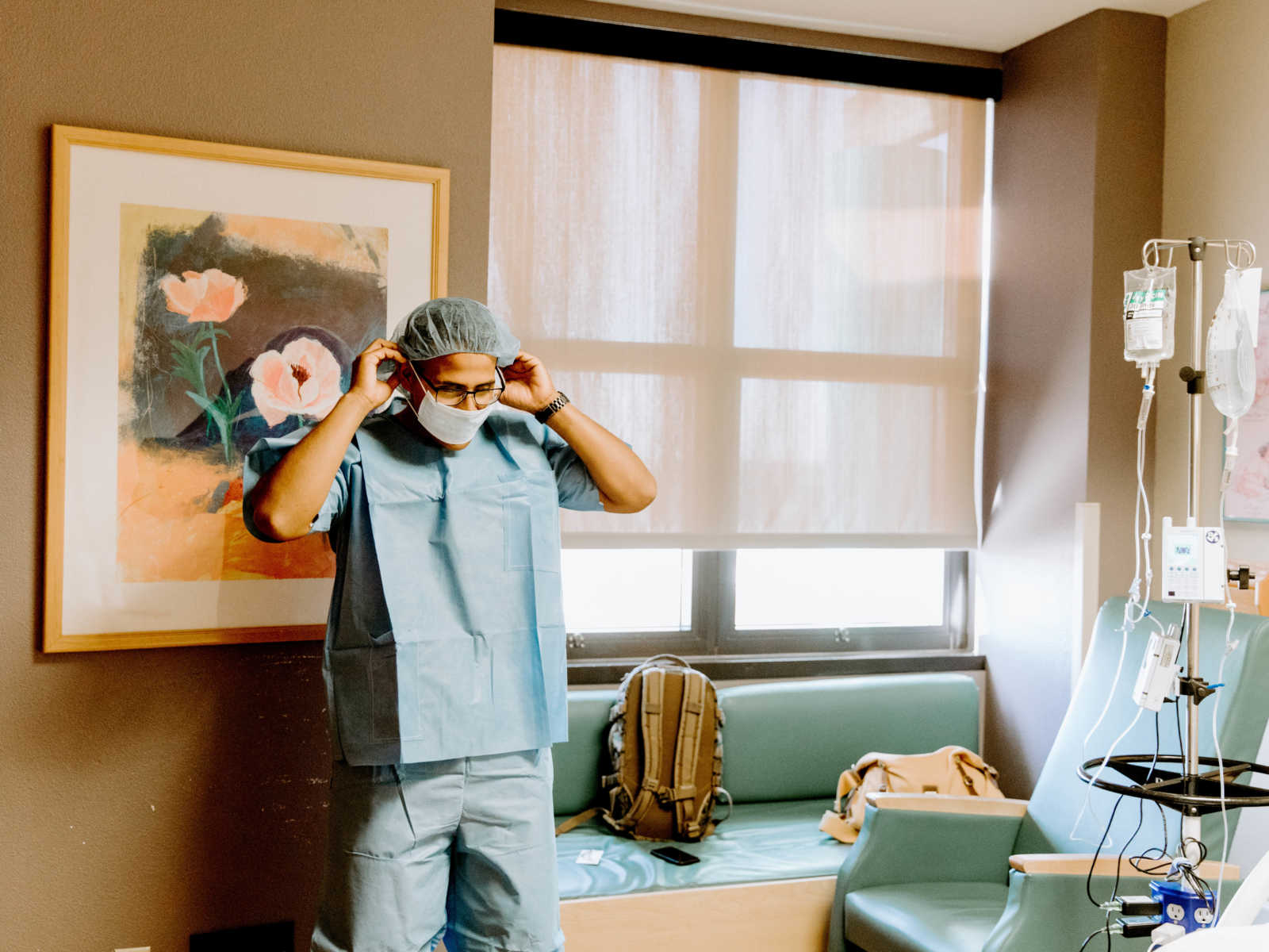 Marine wearing scrubs adjusting his mask in hospital room 