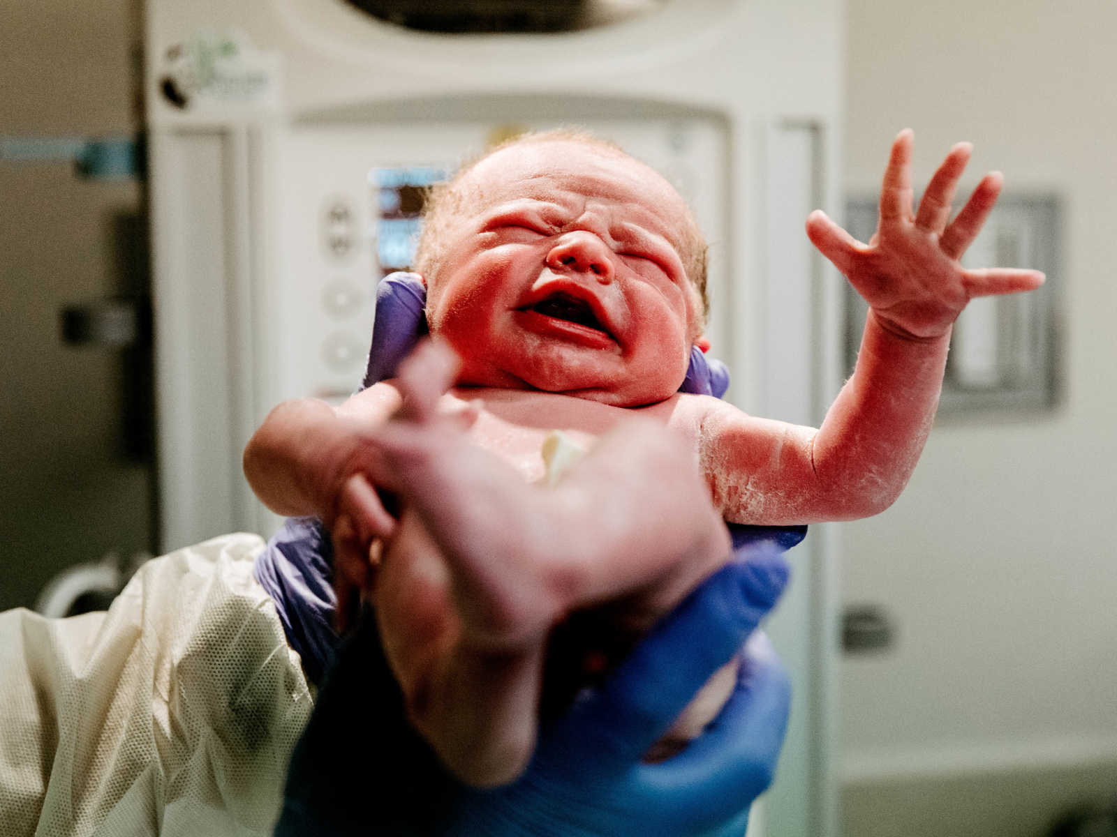 Close up of nurse holding up newborn c-section baby who is crying with hand in air