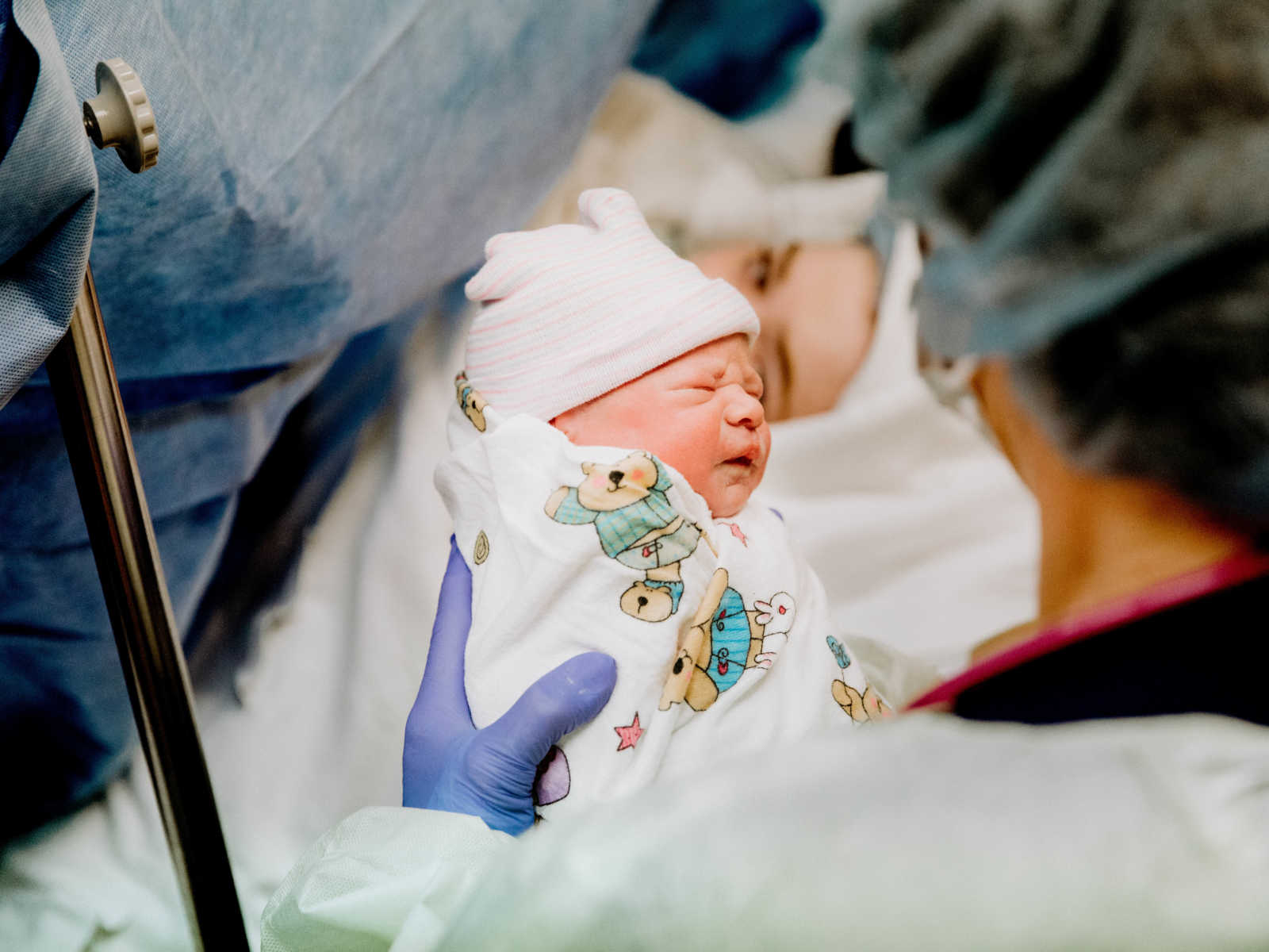 Close up of nurse holding swaddled newborn c-section baby in blanket covered in teddy bears