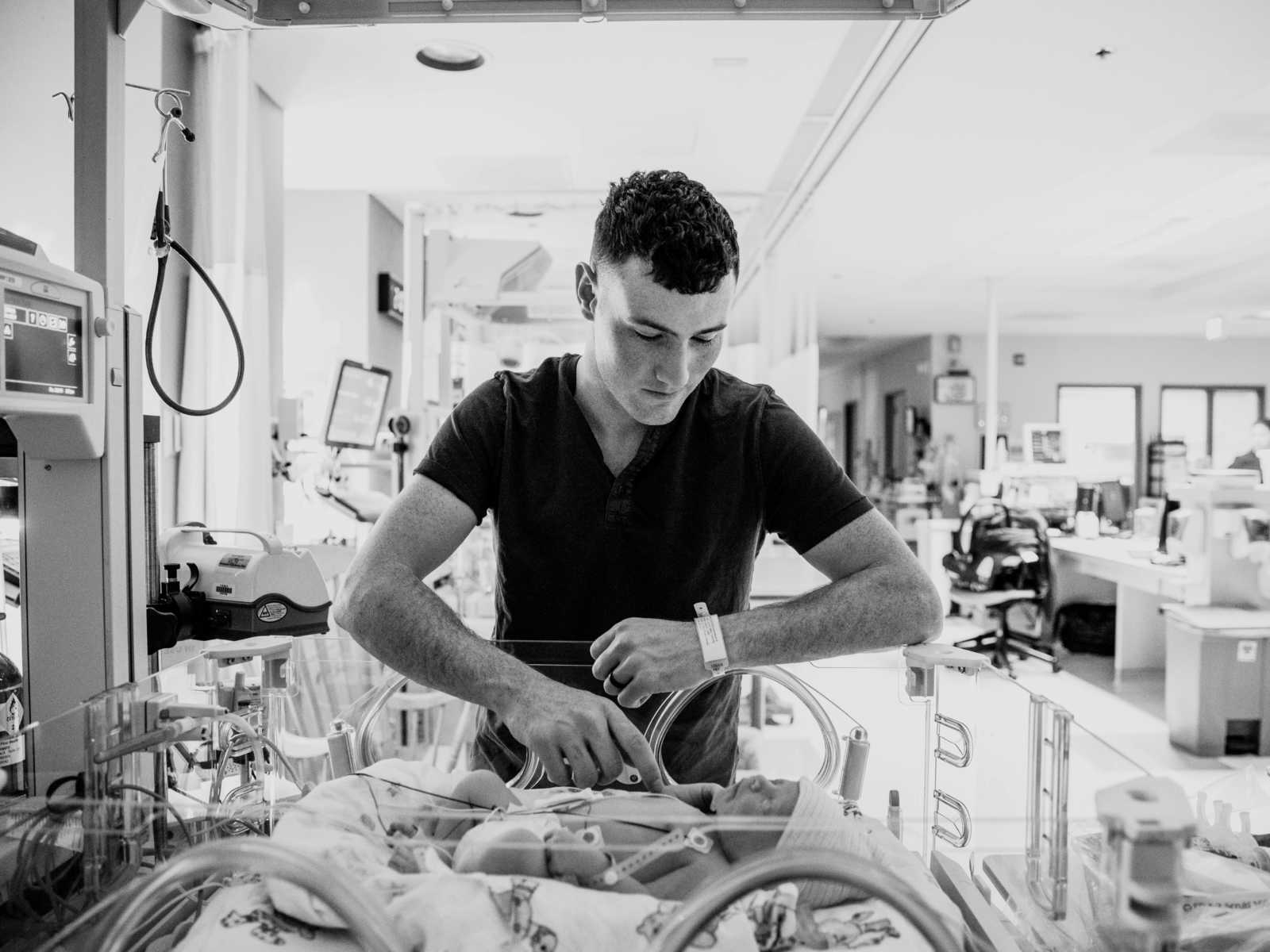 Father of newborn leans over baby and touches it's chest in NICU