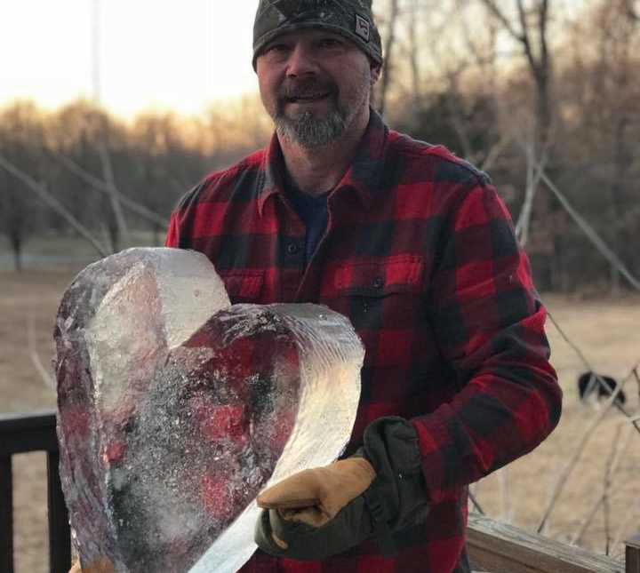 smiling man stands on wooden porch with large piece of ice in shape of a heart