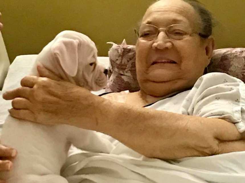 nursing home resident smiles and pets puppy that is in her lap