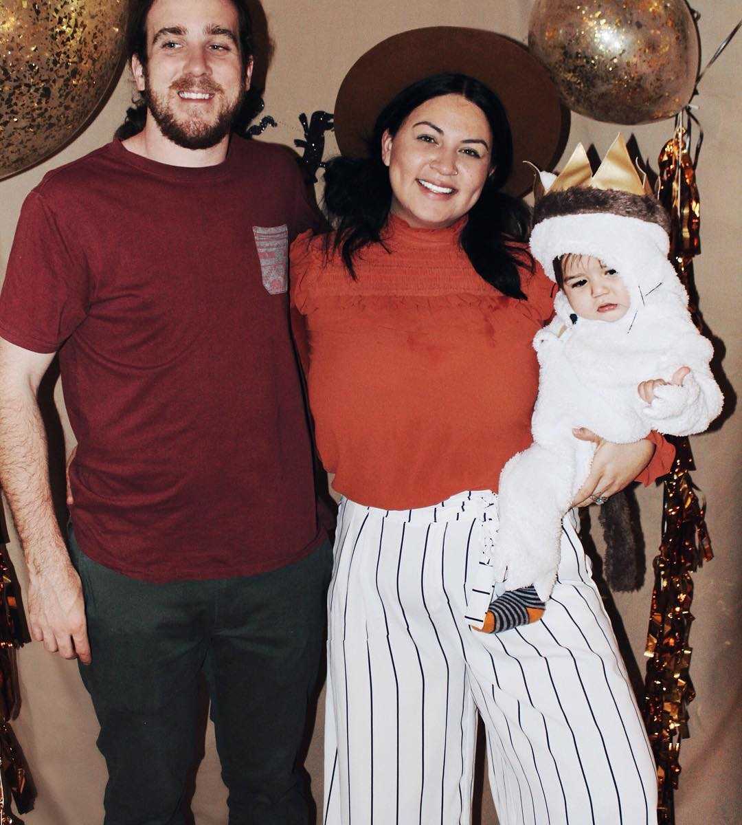 woman struggling with postpartum depression smiles in picture holding baby in costume next to husband