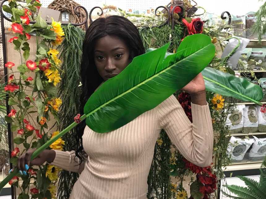 woman holding palm frown across her body in front of shelves of fake flowers