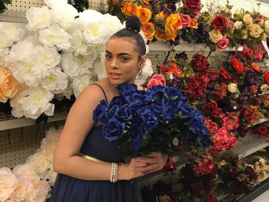woman holding a bouquet of blue roses in front of shelves of fake flowers