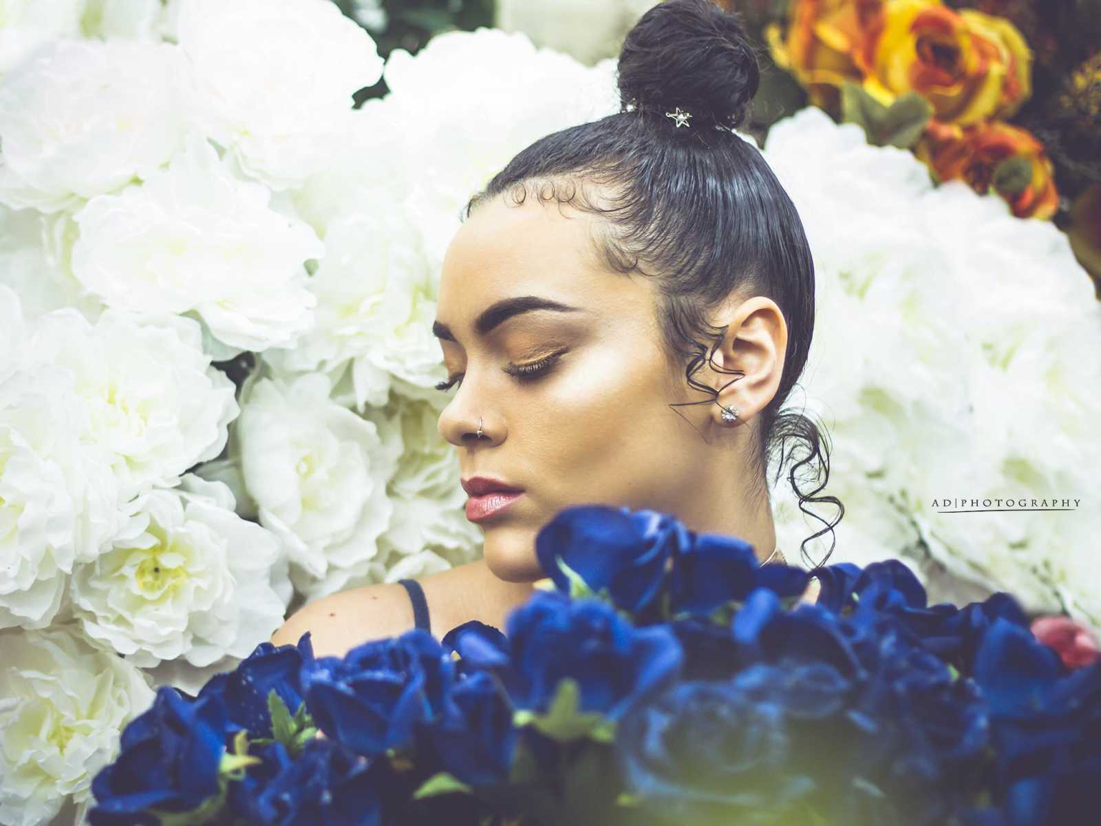 woman holding blue roses with her eyes closed against a backdrop of white flowers