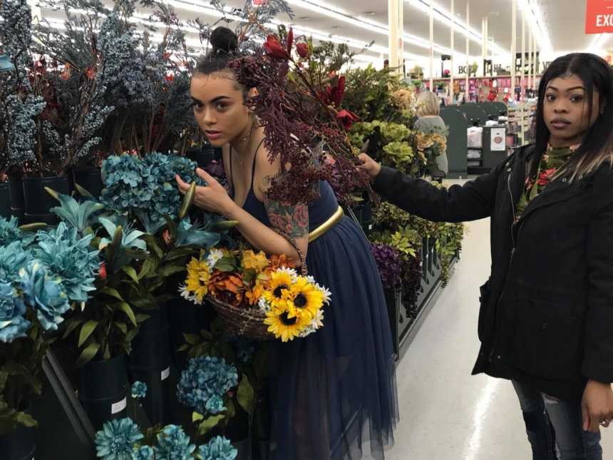 woman leaning over turquoise flowers with basket of sunflowers in arm while another woman holds red flowers next to her head