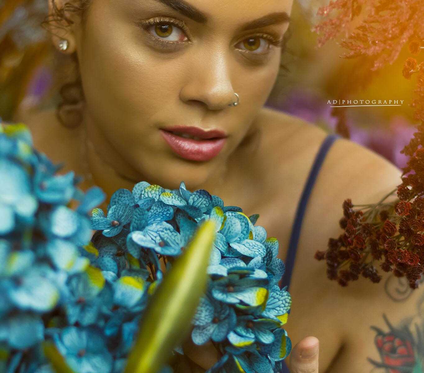 woman behind a bouquet of turquoise flowers and red ones close to her head and shoulder