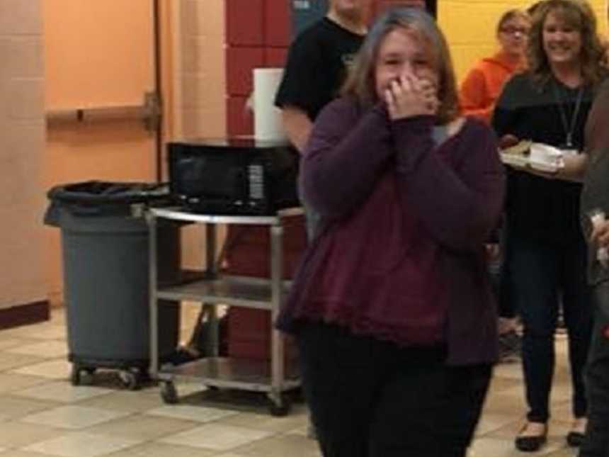 teen girl holds hands over her mouth in cafeteria with people smiling in background