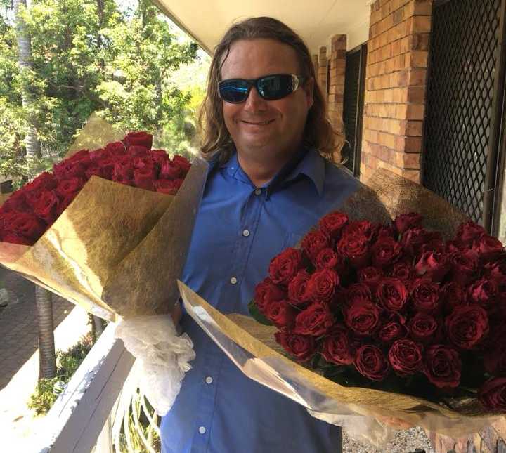 homeless man in blue button down and sunglasses on smile with huge bouquet of red roses in both hands