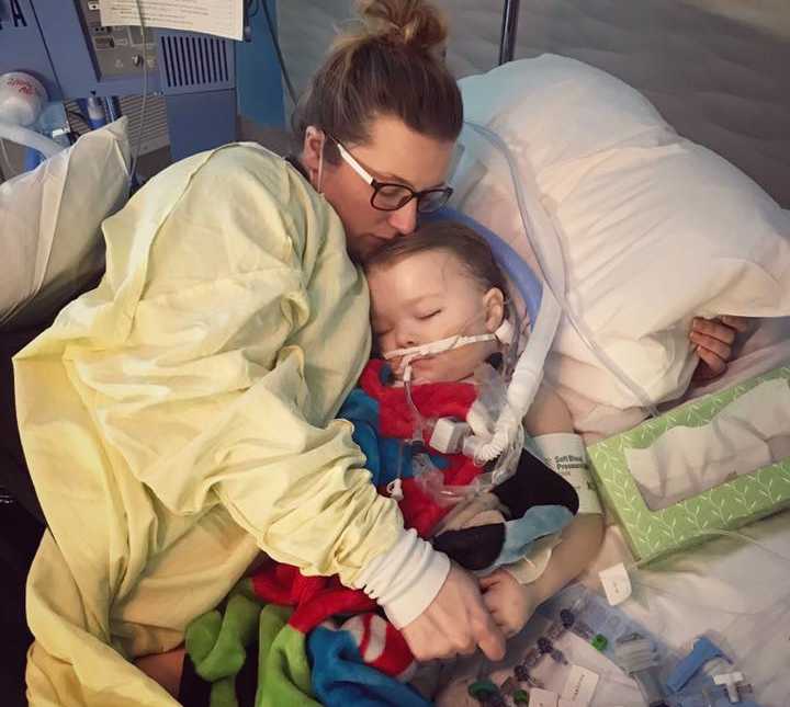 mother in yellow hospital gown laying in hospital bed holding sleeping toddler who has a pump in his mouth in her arms