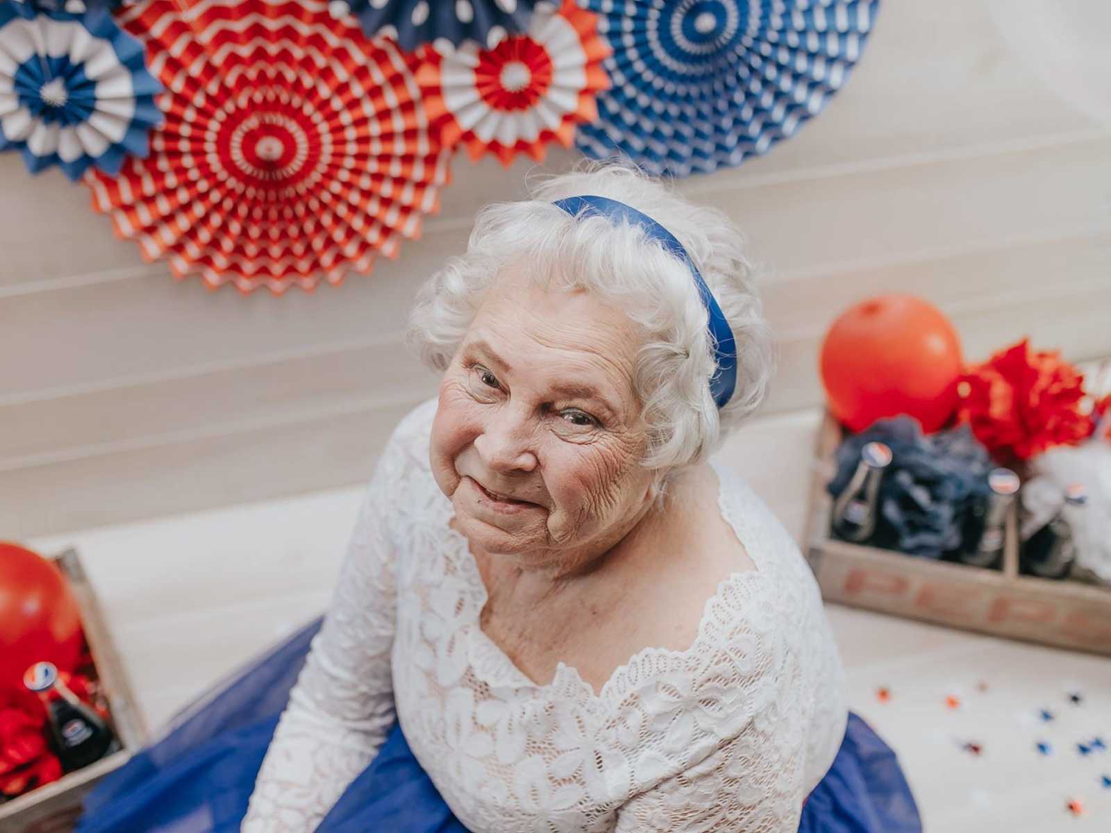 elderly woman looks up smiling with red white and blue decorations all around her