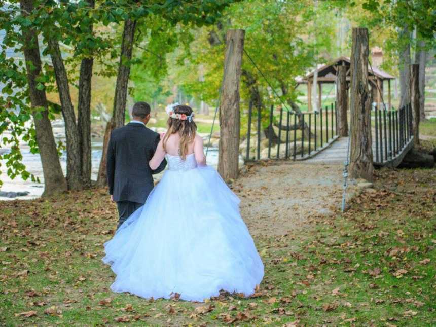 bride in groom arm in arm walking towards a wooden bridge over body of water