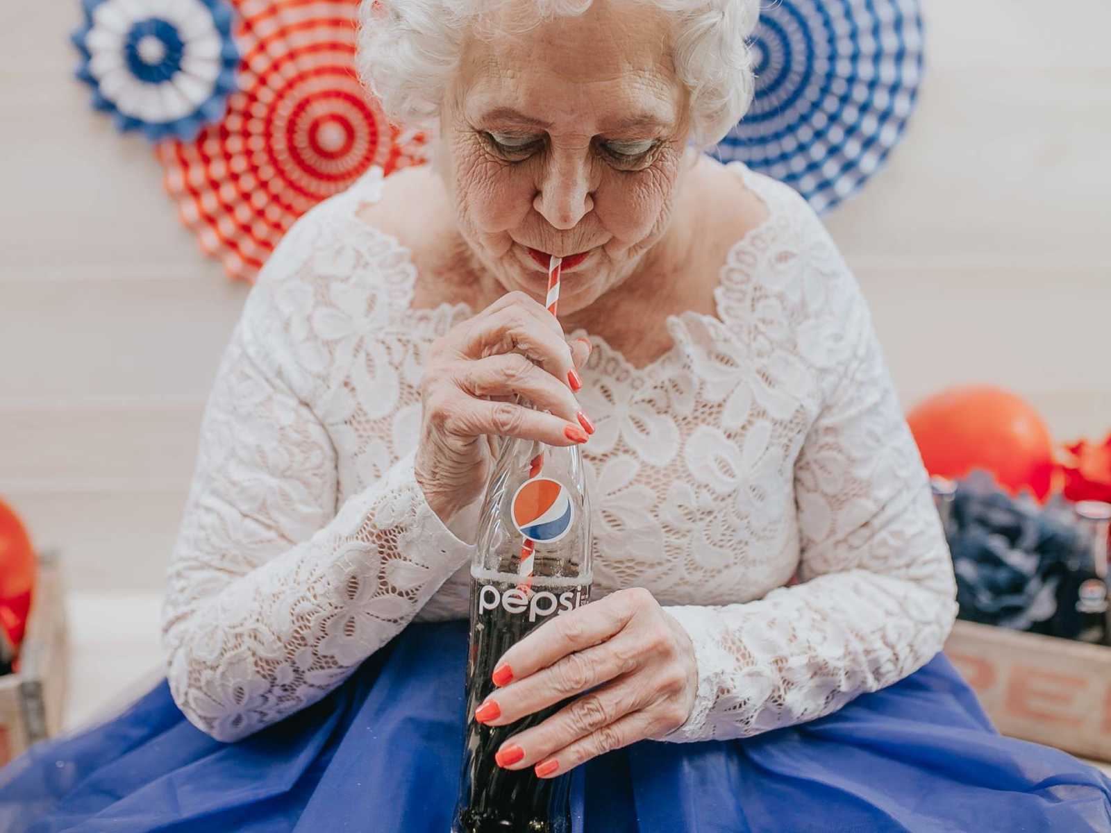 elderly woman takes sip from red and white straw in glass pepsi glass