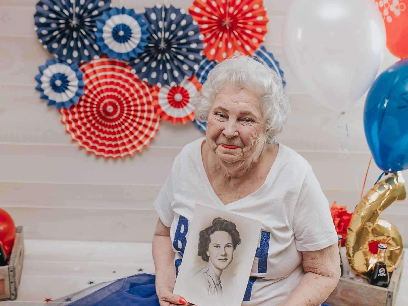 elderly woman smiles while holding drawing of younger self