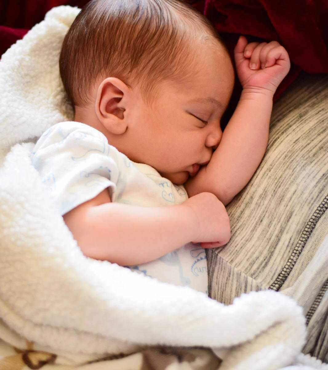 newborn baby wrapped in white fuzzy blanket sleeping