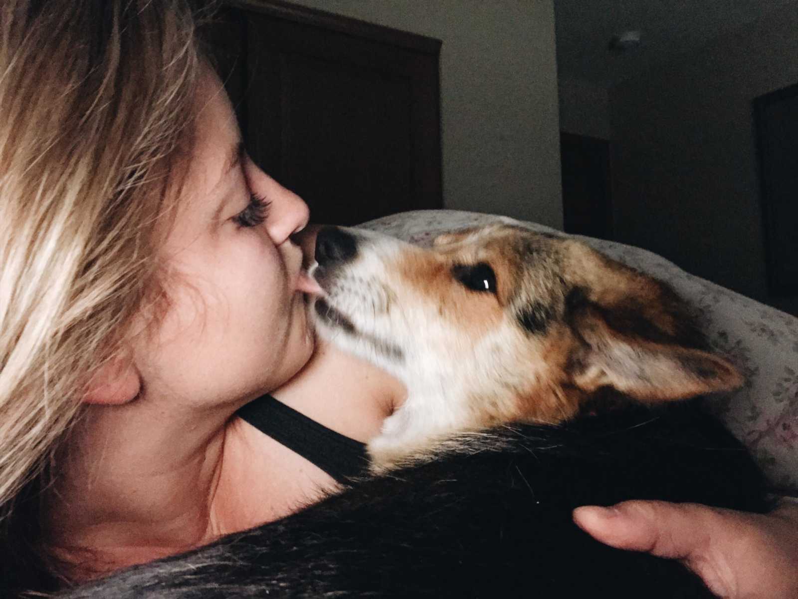dog kissing it's blonde haired owners face while she takes a selfie of it 