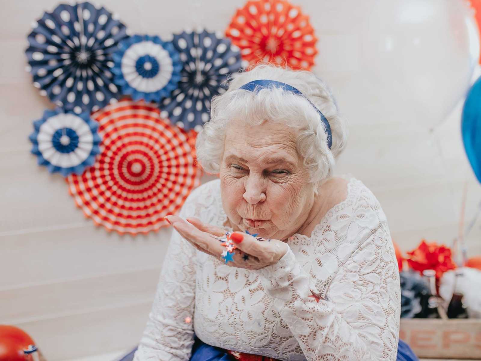 elderly woman blowing red white and blue stars out of her hand