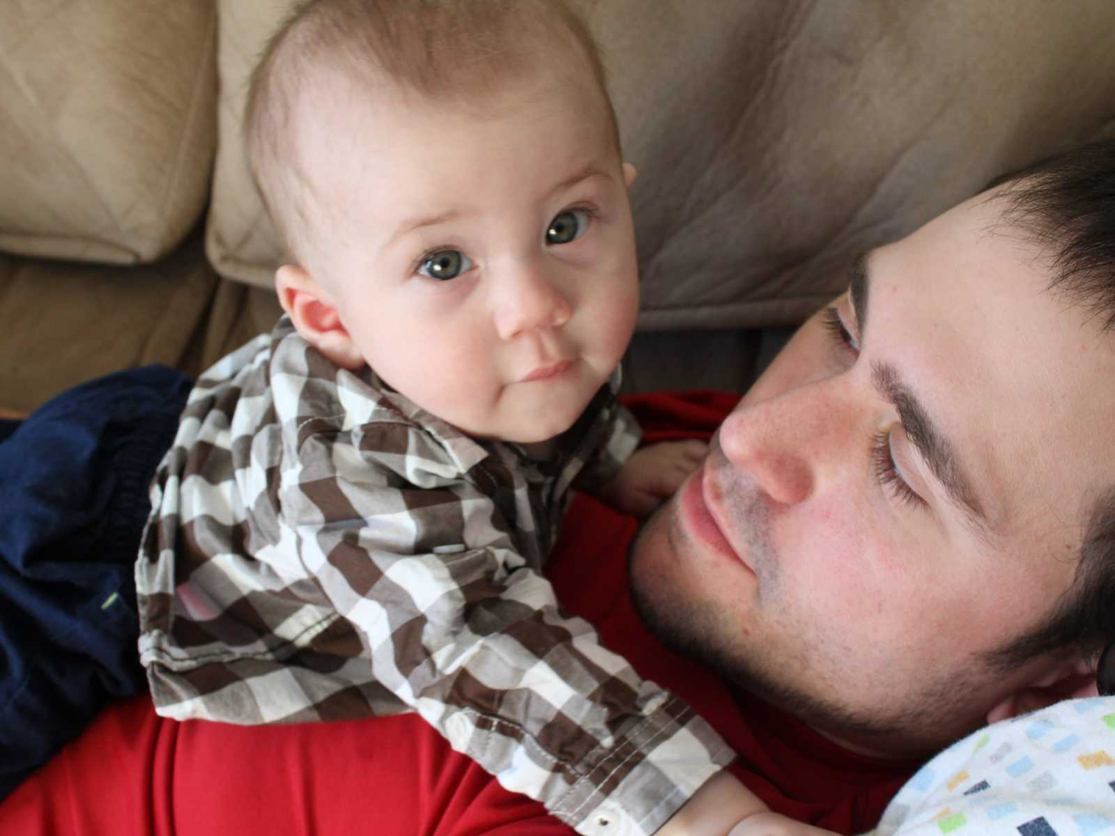 infant looks up while laying on fathers chest on the couch 