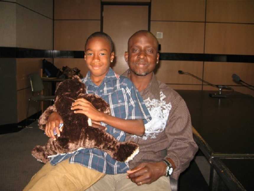 son sits on fathers lap smiling while holding brown stuffed animal