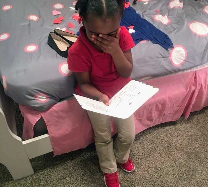 little girl reads a card while leaning on her bed with hand over her face