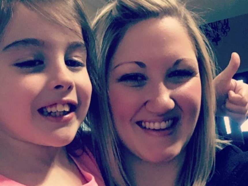 Toddler with rare disease smiles with a thumbs up in selfie with mother