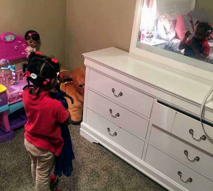 little girl holds up purple dress in front of mirror in her bedroom