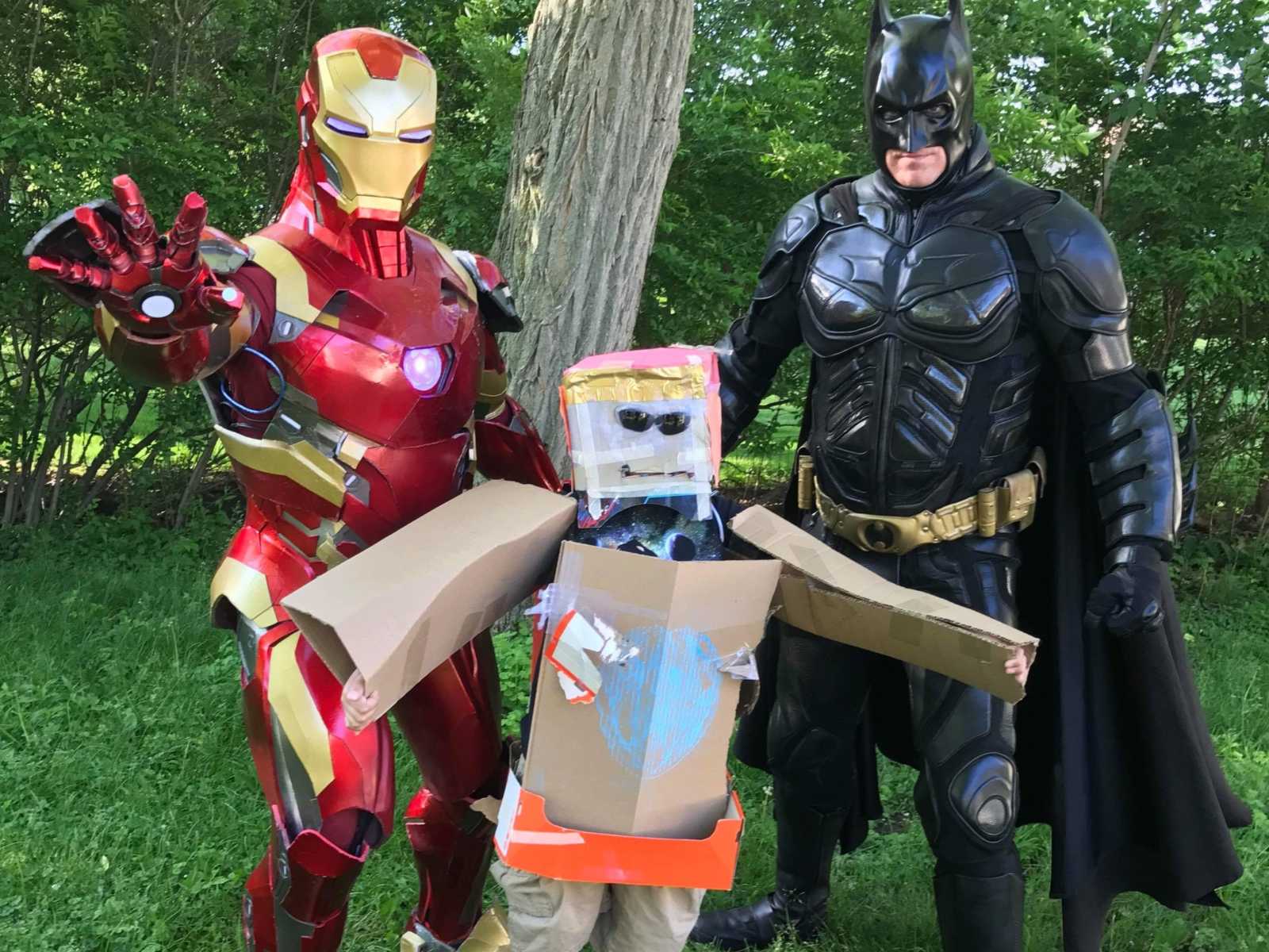Little boy with cancer wears homemade iron man suit made out of cardboard next to iron man and batman