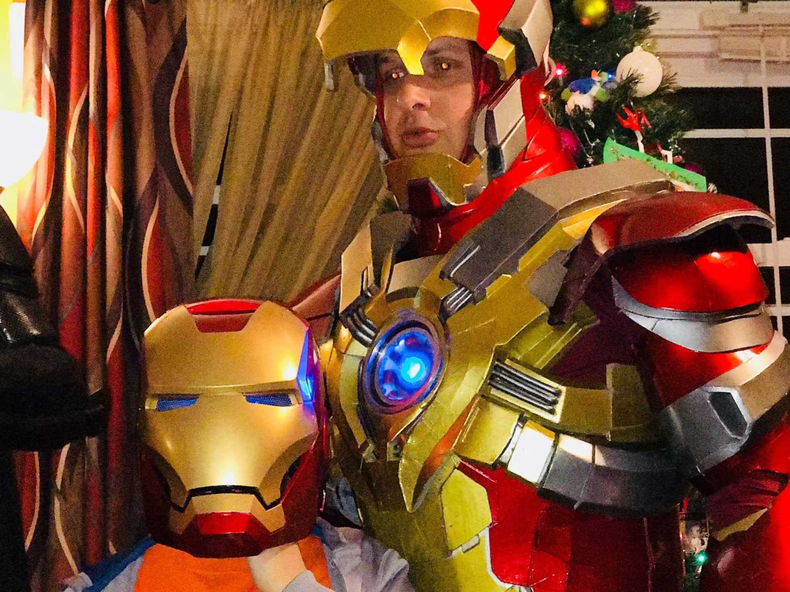 Man in iron man suit stand next to boy with cancer who has iron man helmet on