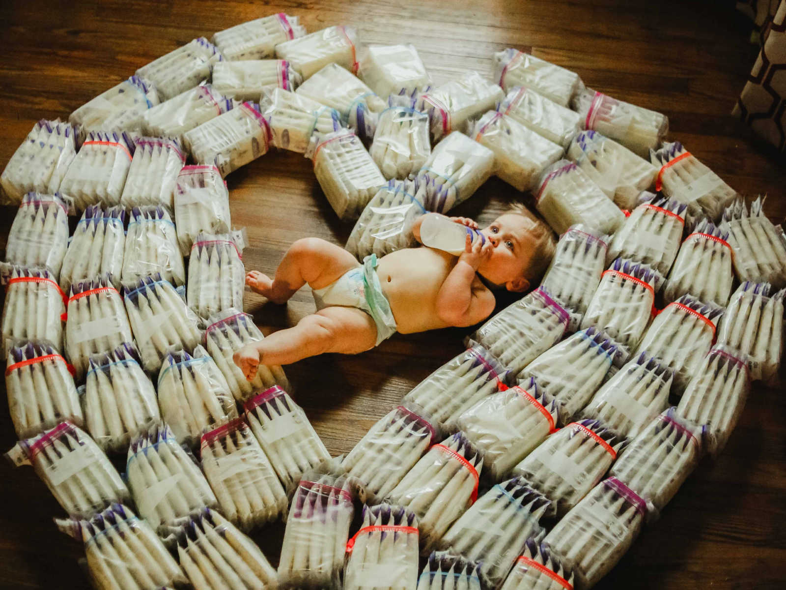 Baby lying on the floor drinking breastmilk out of a bottle in middle of diapers shaped in heart