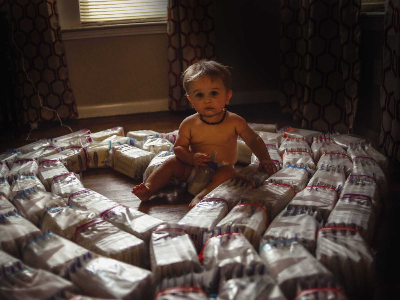 Infant sitting up on the floor with bottle full of breastmilk in the middle of diapers shaped in heart