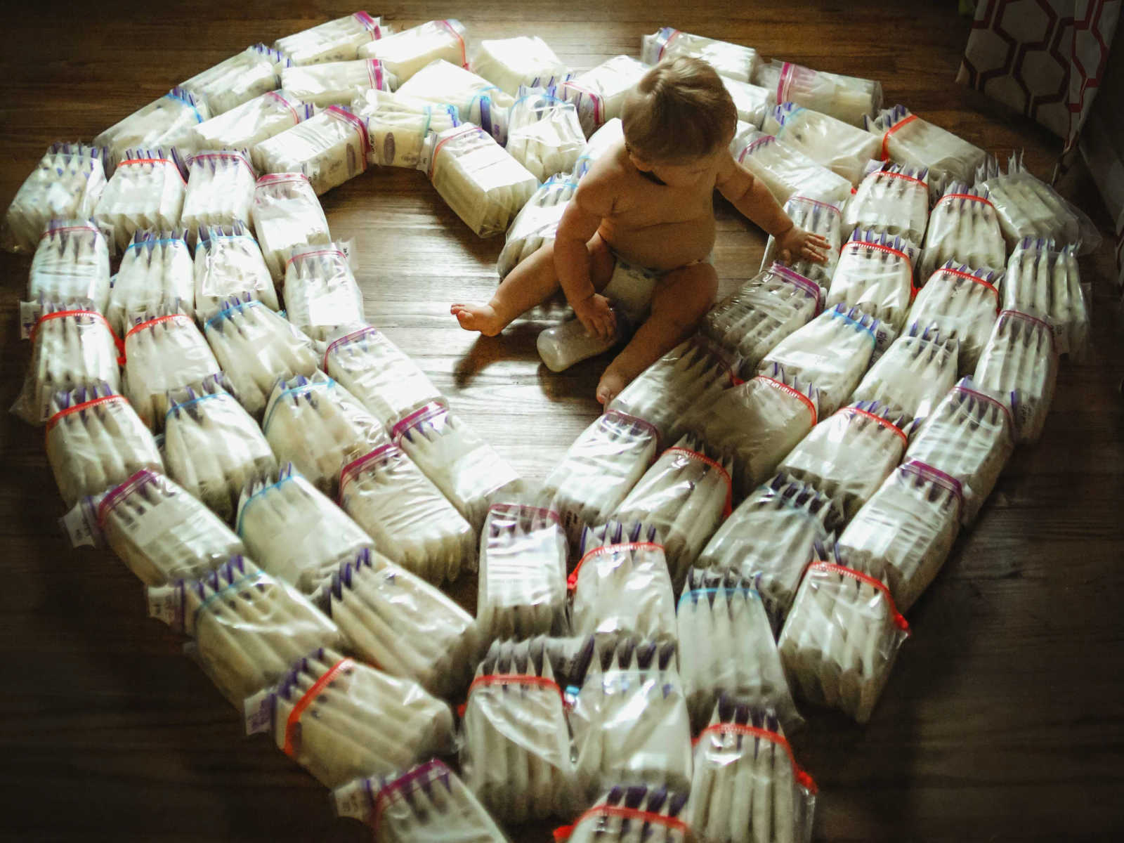Aerial view of baby sitting in the middle of diapers shaped in heart with one hand on a diaper and other on bottle