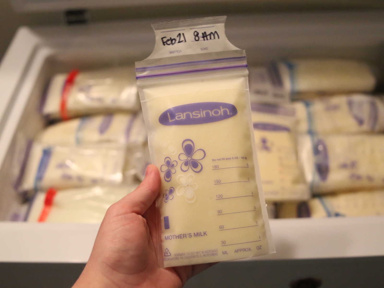 Close up of someone holding bag of breastmilk with stacks of breast milk in freezer in background