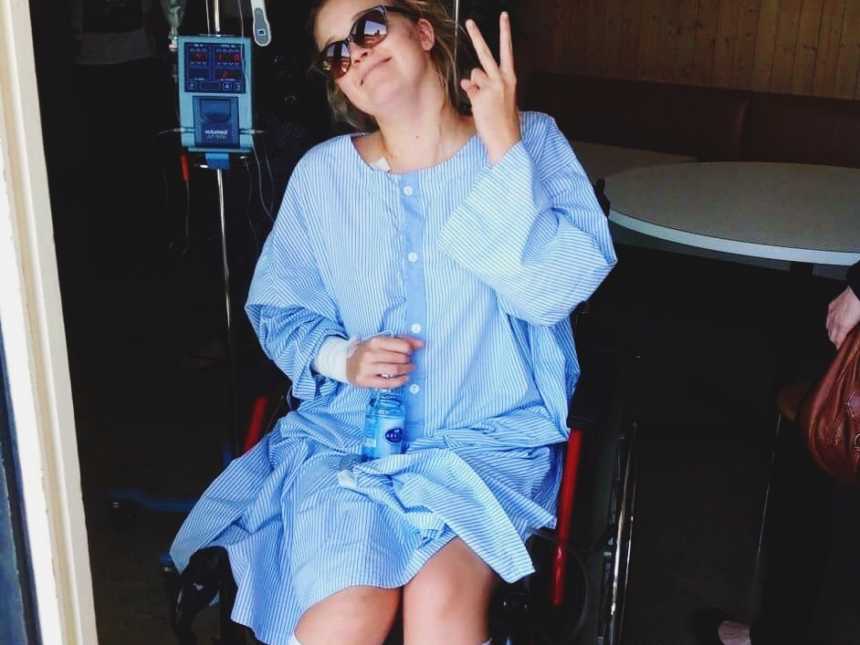 Paraplegic woman sitting in wheelchair wearing sunglasses holding up a peace sign 