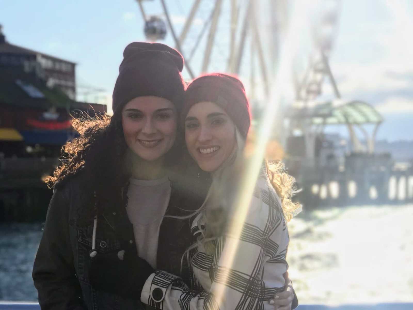 same sex couple in red beanies smiling with ferris wheel in background