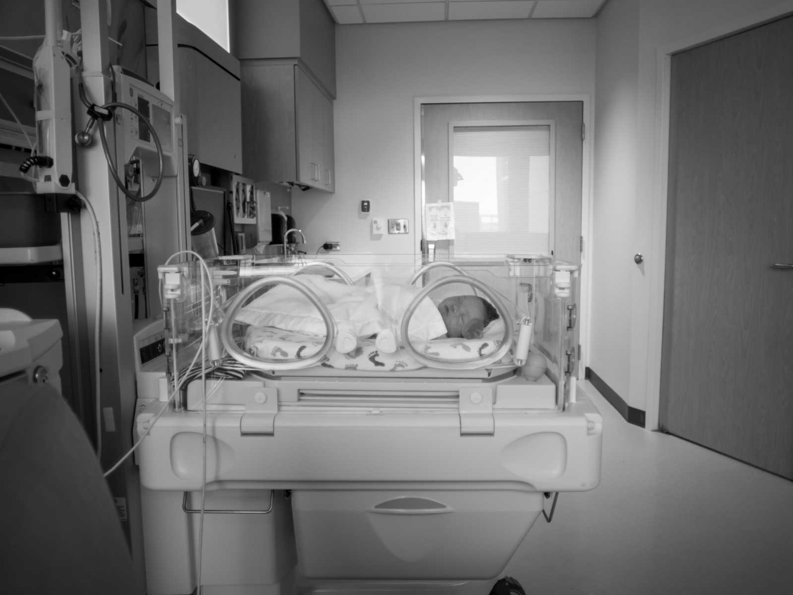 newborn swaddled in blanket in baby hospital bed hooked up to machines in black and white