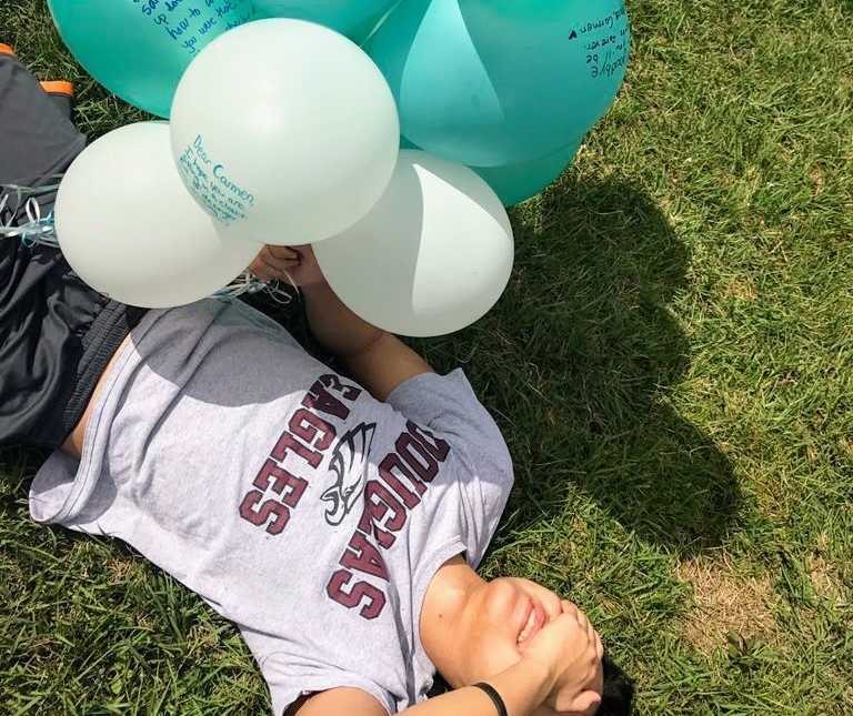 Teen boy lies on the grass crying holding balloons for teen who lost her life in Parkland school shooting in Florida