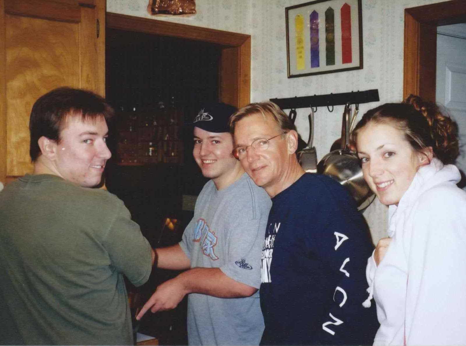 father stands in kitchen smiling next to daughter and two sons