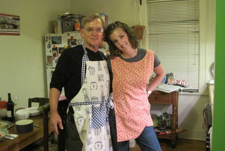 man and woman stand in kitchen with arms around each other wearing aprons