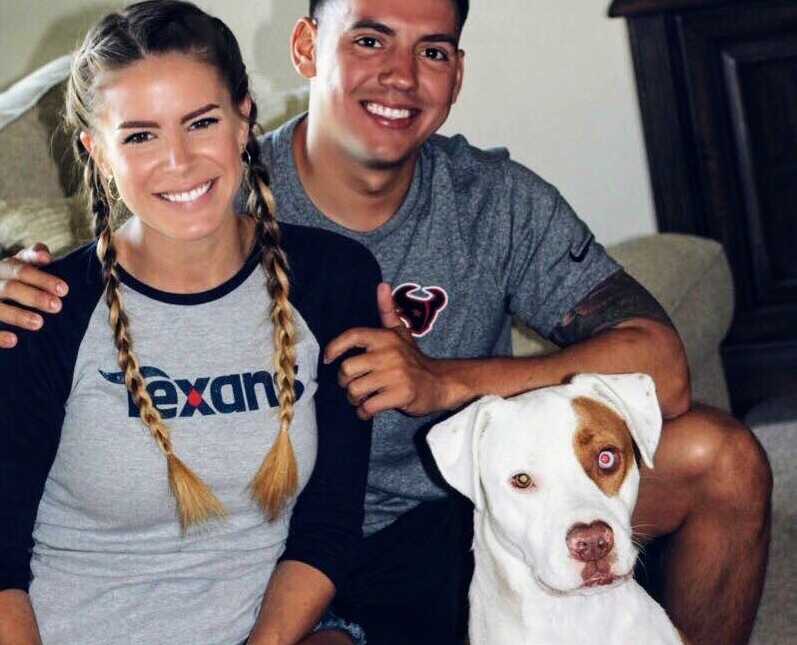 Couple sits on couch smiling with their dog sitting in front of them