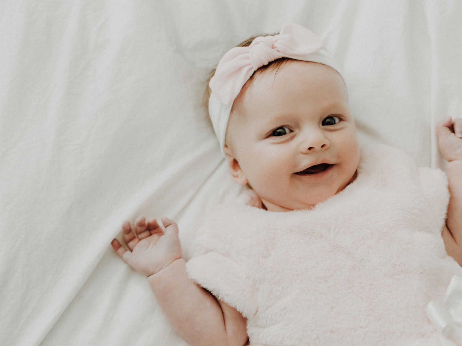 baby girl smiling in a pink fuzzy top and light pink headband with a bow