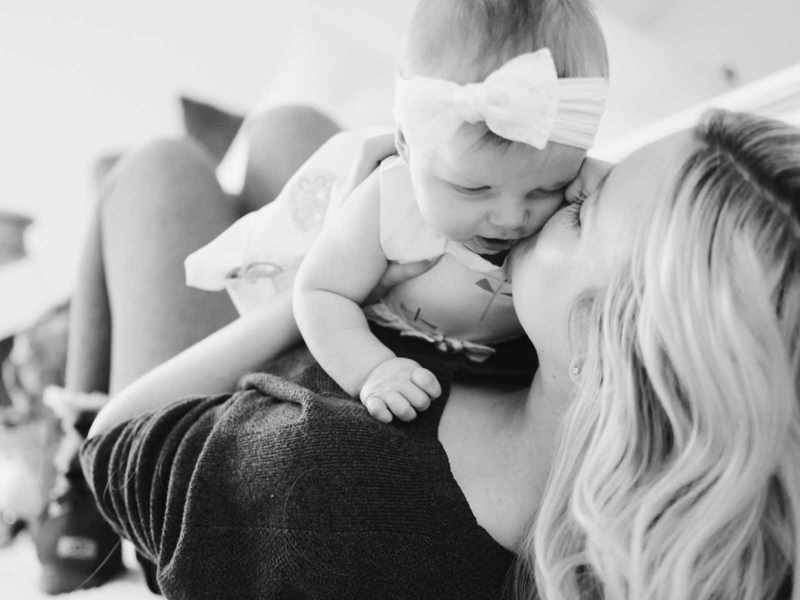 mother holding baby girl on her chest giving her a kiss on cheek