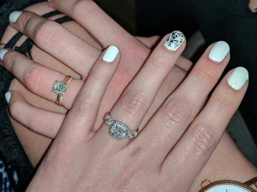 Engaged women’s hand with white nail polish placed on top of another engaged women’s hand with white nail polish