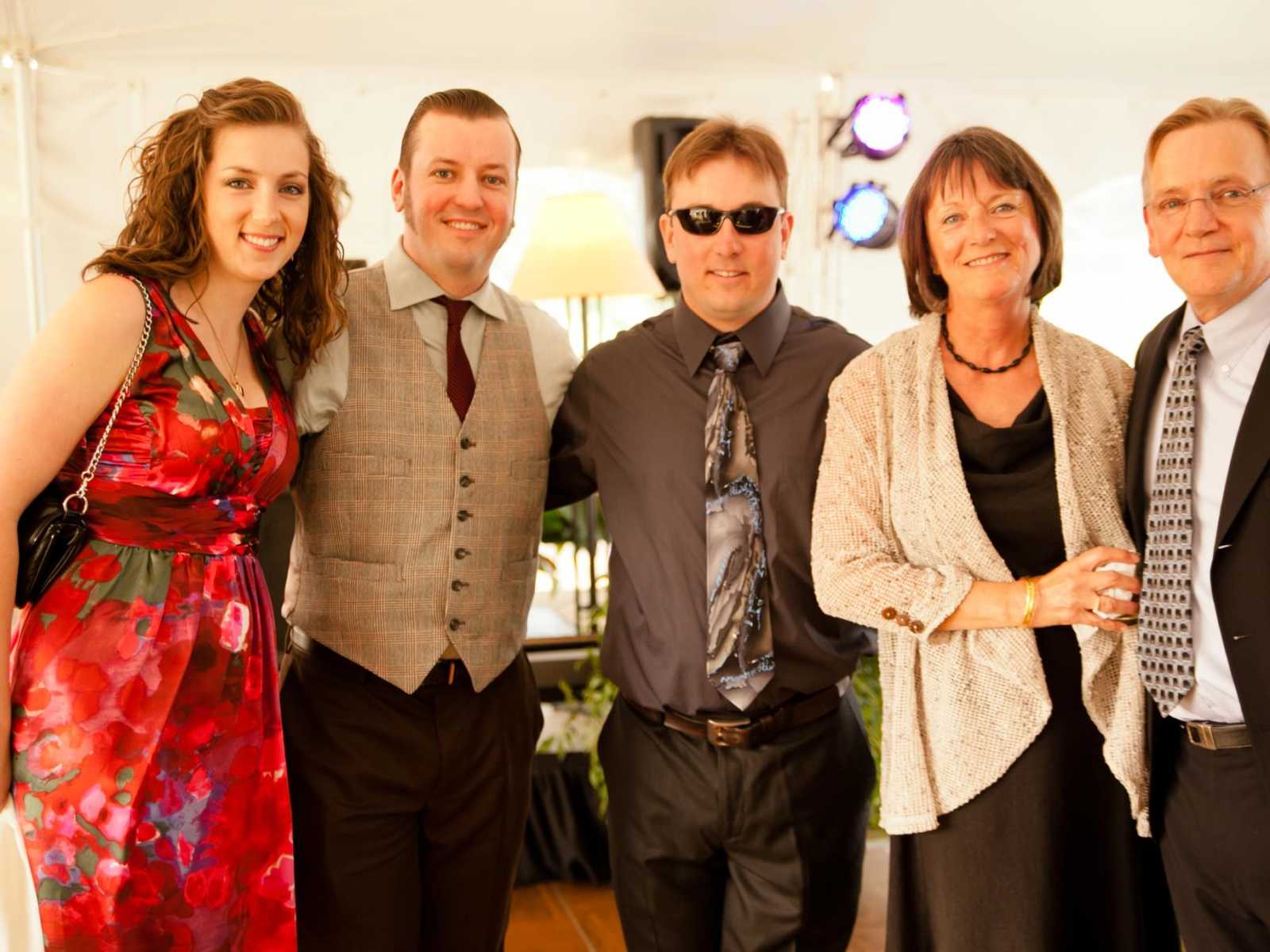 retired father smiles standing arm in arm with wife, two sons and daughter