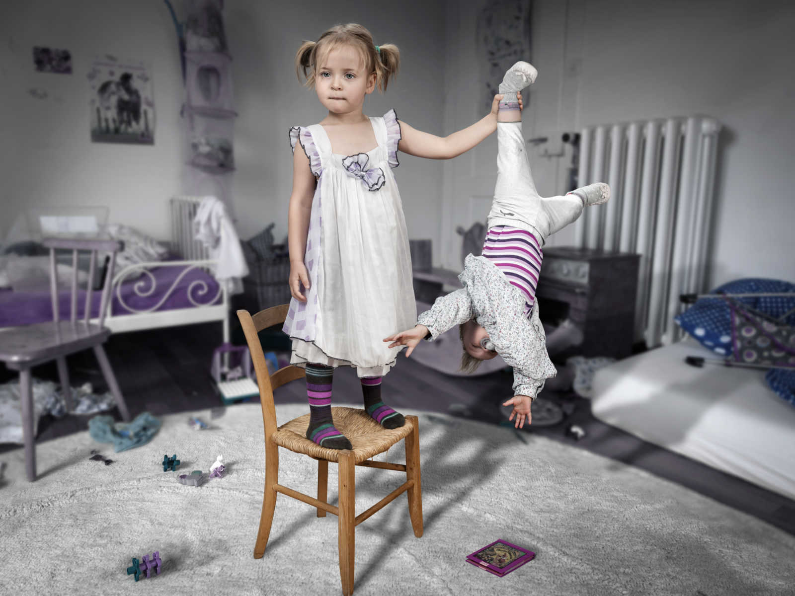 young girl stands on chair in animated bedroom while holding her younger sibling upside down by a leg