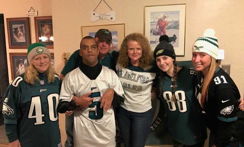 father holding up cerebral palsy son with four other women who are all wearing Philadelphia eagles jerseys